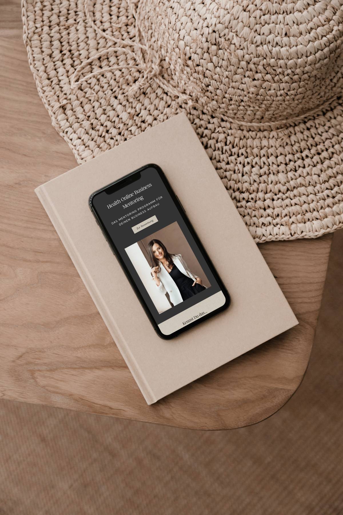ein Handy Mockup mit Screenshot der Website von Hannah Willemsen liegt auf einem braunen Holzstuhl, daneben ein Strohhut