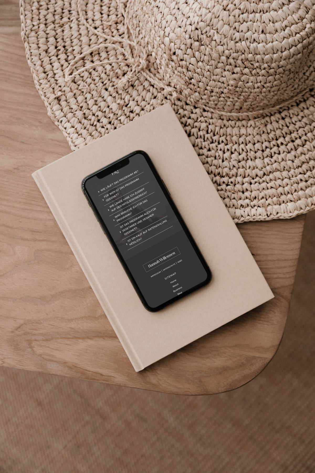 ein Handy Mockup mit Screenshot der Website von Hannah Willemsen liegt auf einem braunen Holzstuhl, daneben ein Strohhut