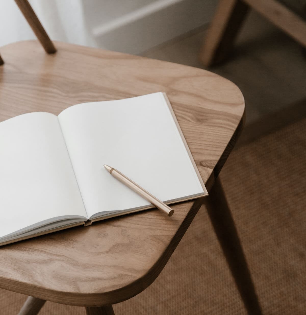 ein Notizheft aufgeschlagen mit weißen Seiten auf einem brauen Holzstuhl