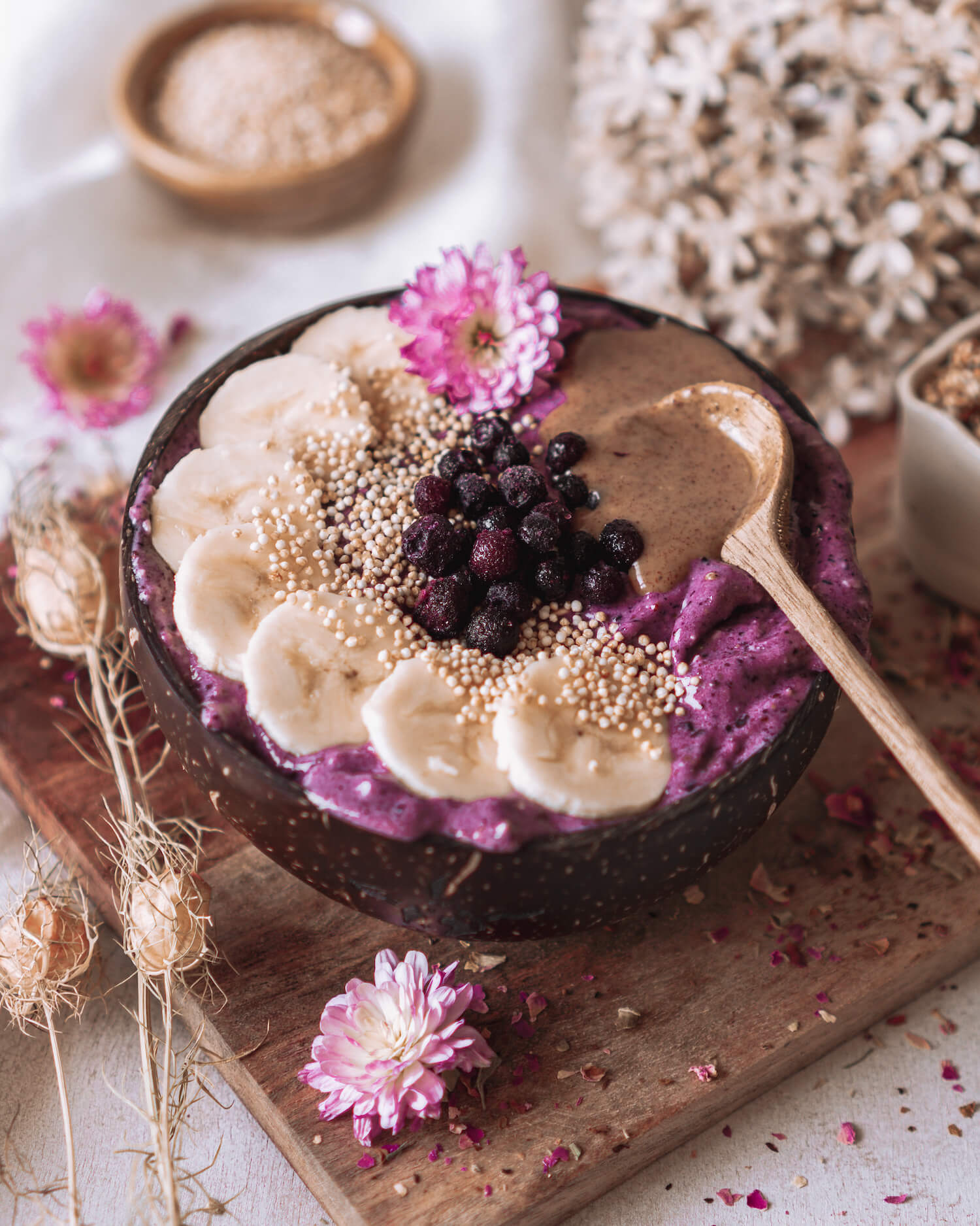 eine lila Smoothie Bowl garniert mit Banane, Heidelbeeren und Nussmus in einer Kokosnussschale