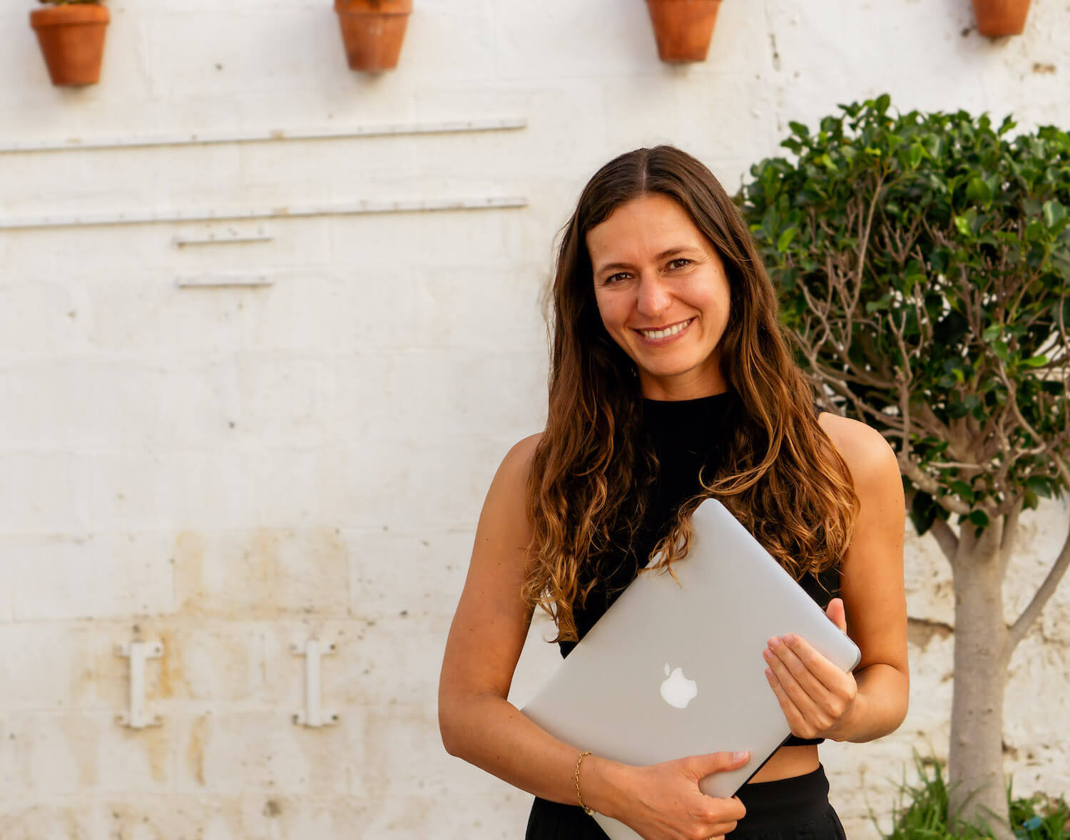 Frau hält ein silbernes MacBook in den Händen und lächelt